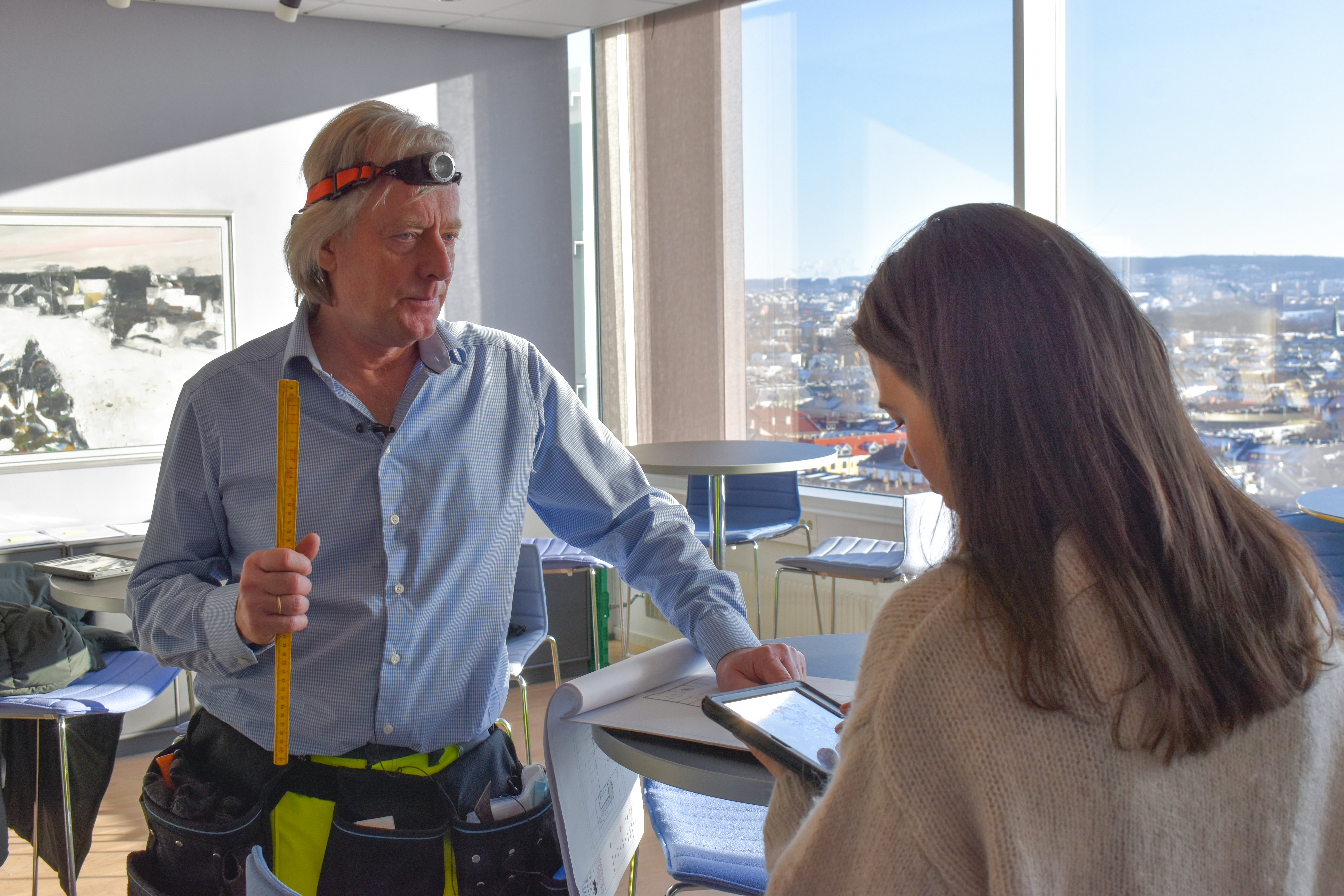 Mann holder tommestokk og kvinne notere på et nettbrett