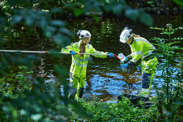 To personer i vernelklær tar vannprøver i elv